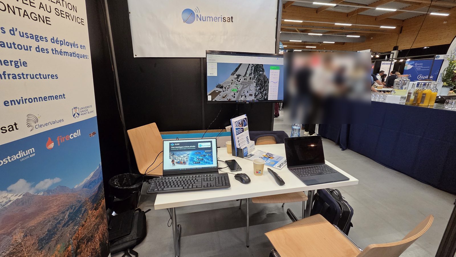 The Numerisat stand at the Domaines Skiables de France congress: the ELIAN 3D digital twin of a ski resort on the big screen, laptops running the ELIAN demo on the table.